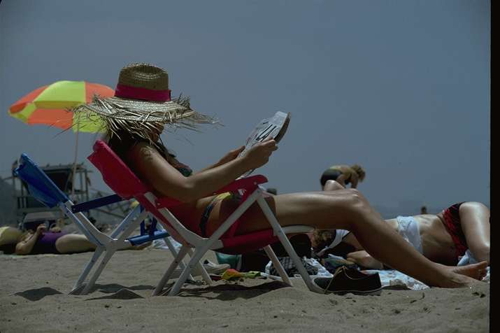 Mujer con sombrero, sentada leyendo al sol